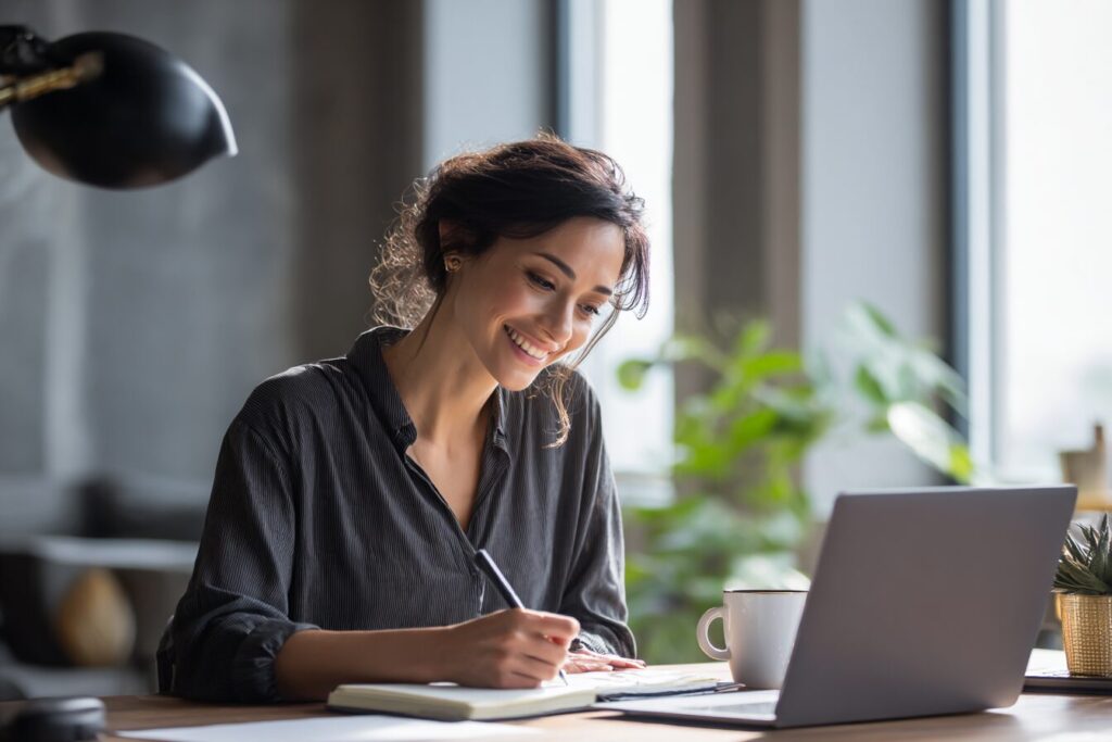 Ultra-realistic 4K image of a young Filipino professional working from home, seated at a tidy desk with a laptop open. The person is dressed in smart-casual (blouse or polo shirt), smiling with a confident posture, and taking notes on a notebook beside the laptop. Subtle natural lighting from a window, minimal décor like a plant or mug, creating a fresh, professional, and encouraging vibe. The scene should capture self-assurance and readiness to grow as a Virtual Assistant.